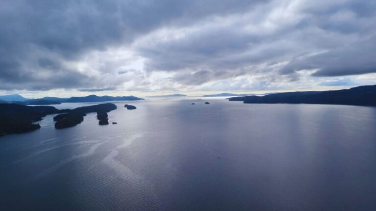 A calm aerial view of the Gulf Islands in British Columbia, with soft clouds, blue water, and distant islands fading into the horizon.