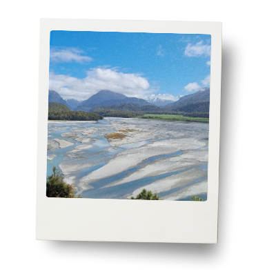 The Dart River in Queenstown New Zealand - a sweeping view with the river winding it's way back into beautiful mountains with a blue sky.