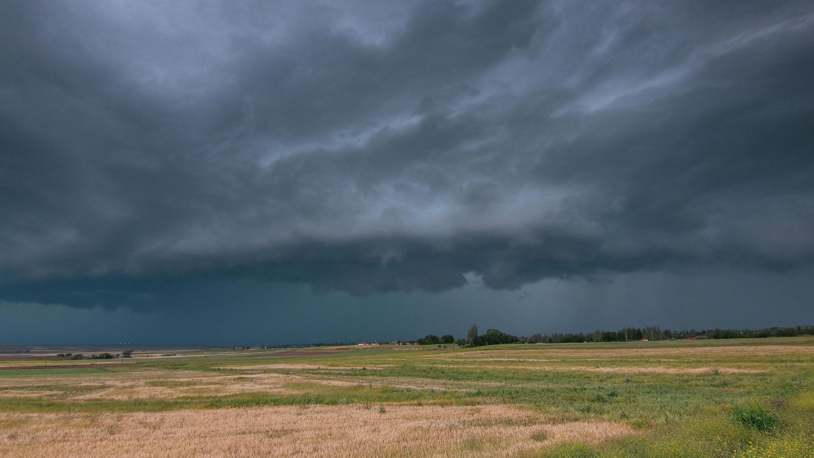 Approaching storm over open farmland, with low clouds and a still, expansive horizon.